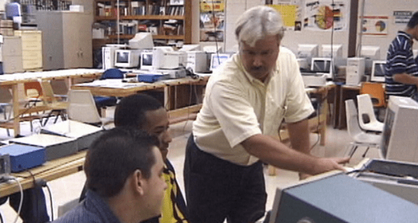 Male teacher in adult computer class room with two male students looking at a screen