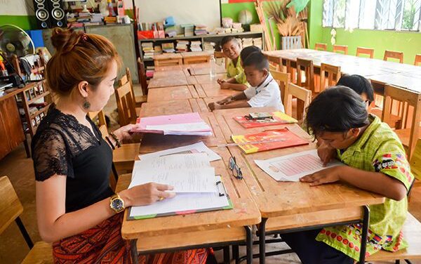 Teacher sitting at desk with children in class