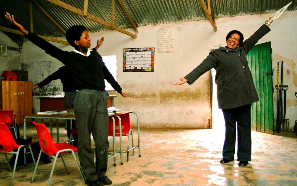 A teacher and pupils with arms spread wide