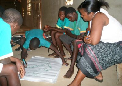 Student adding to a large diagram on a page with other students and teacher looking on