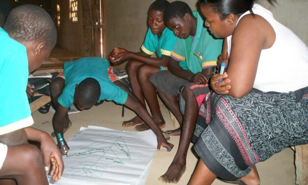 Student adding to a large diagram on a page with other students and teacher looking on