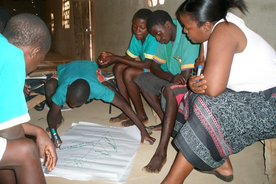 Student adding to a large diagram on a page with other students and teacher looking on