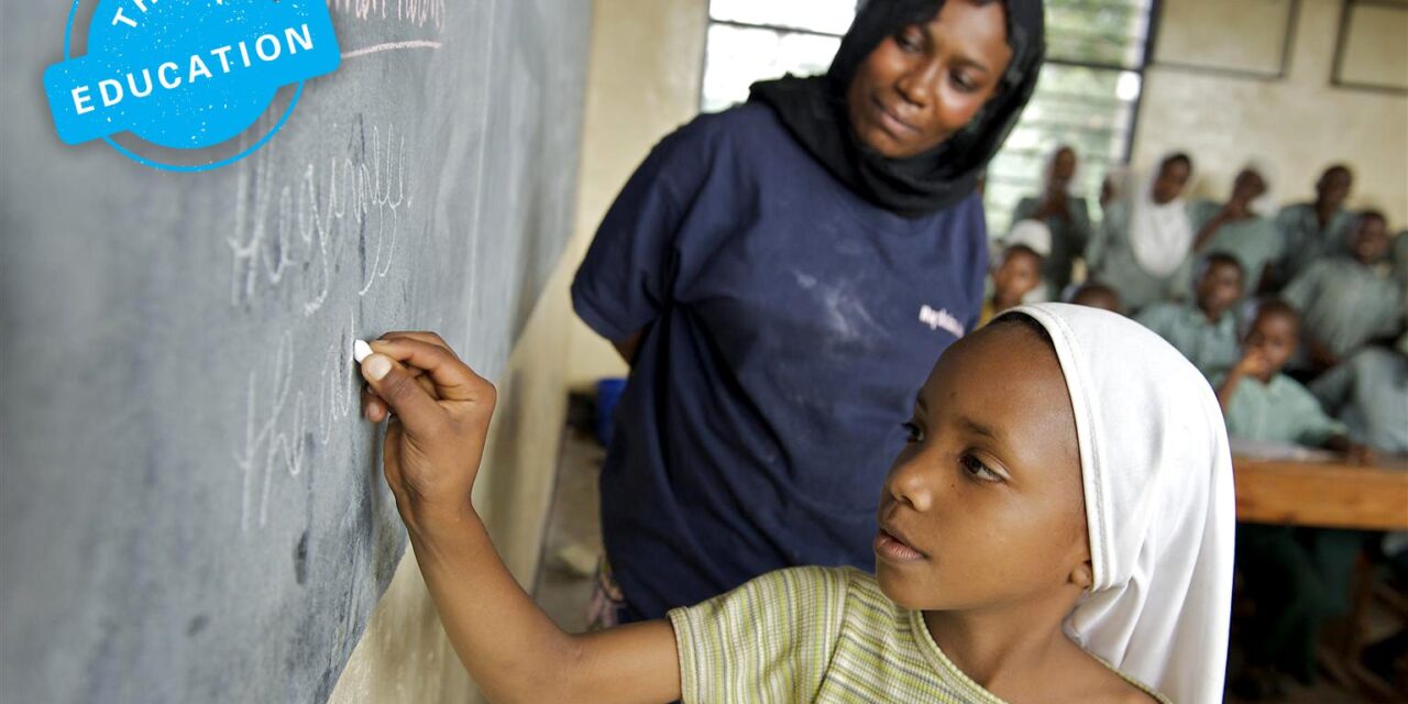 Student writing on a blackboard with teacher