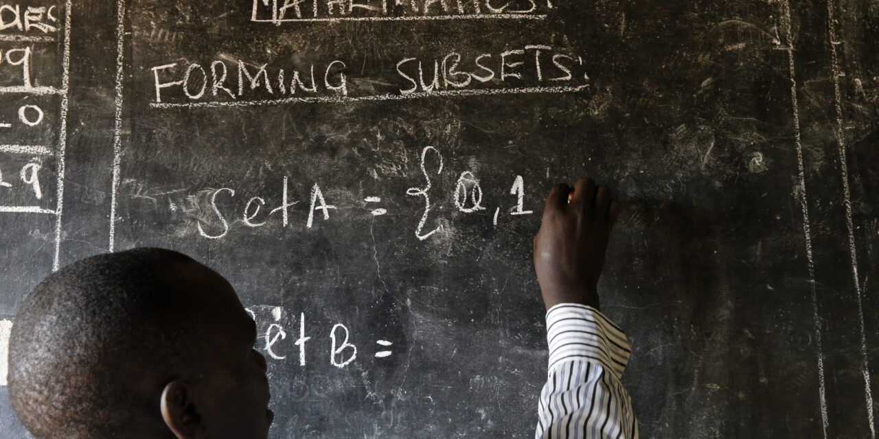 A teacher writes maths formulas on a blackboard at a school. Image Credit_Philippe-Lissac_Godong_Panos-Pictures