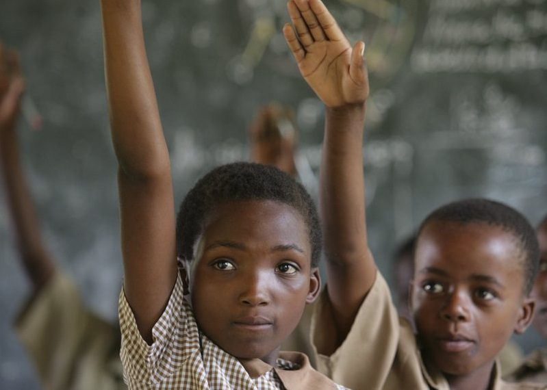 primary school children with hands up in in class