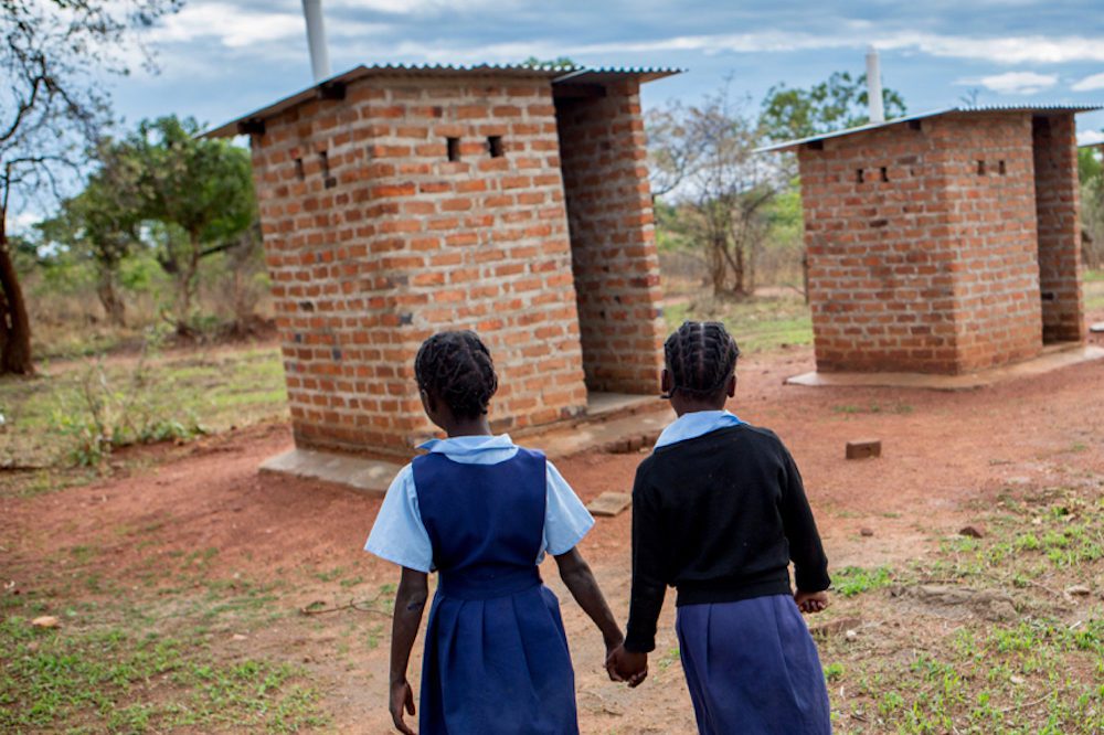 primary age school girls walking hand in hand towards a school toilet block