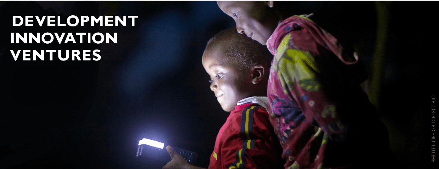 Two boys in the dark with a torch shining light into their faces. Development Innovation Ventures