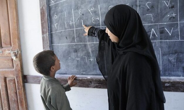 A teacher pointing at the blackboard with a child