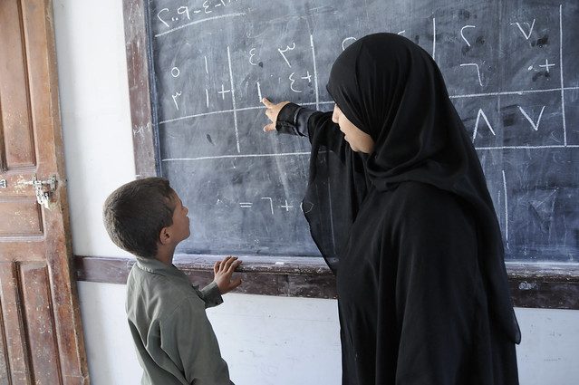 A teacher pointing at the blackboard with a child