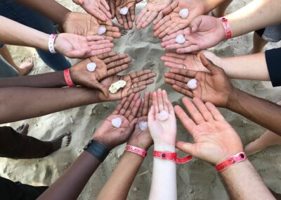 A ring of hands all with palms upturned, different coloured skin, some with a heart shape in the palm, some with nothing, one with coral