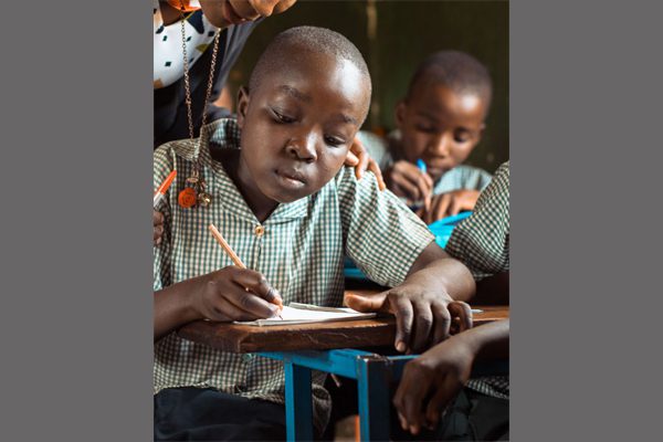Primary school child writing in class with a teacher supporting and looking over their shoulder
