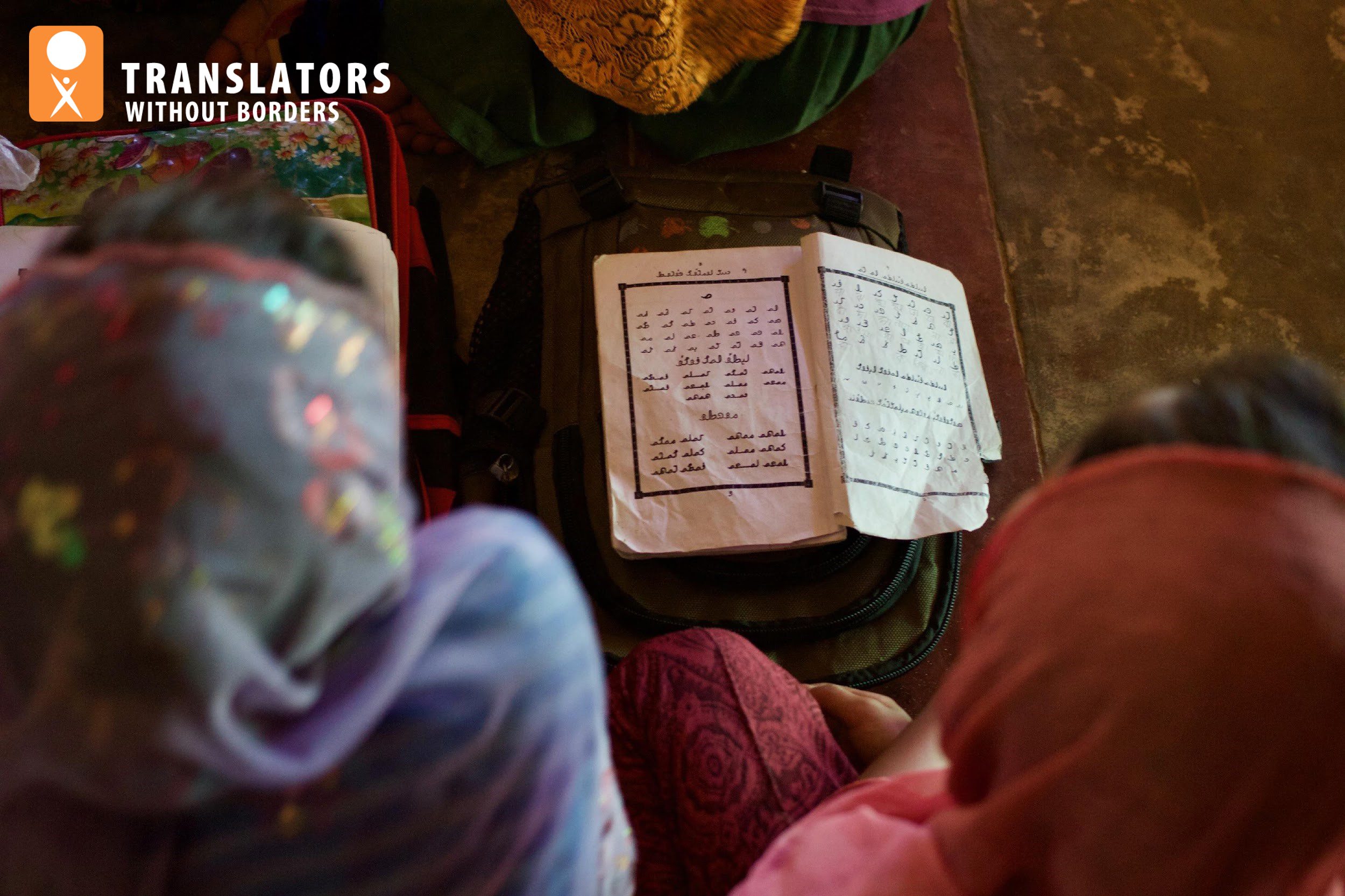 Translators without borders. Looking over the heads and shoulders of two girls looking at a book written in script.