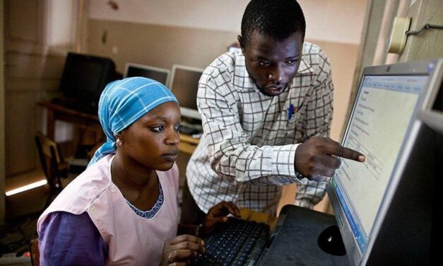 A male pointing at a computer screen with a female seated at the keyboard