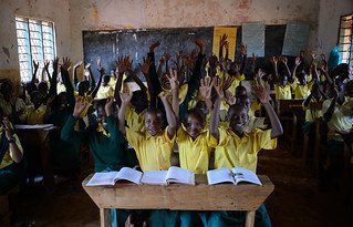 Children in yellow uniform shirts with their hands raised in class