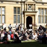 Conference delegates sitting on grass at lunchtime in the sunshine of the quod at Examination Schools