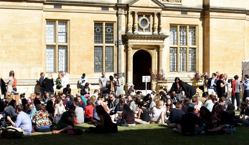 Conference delegates sitting on grass at lunchtime in the sunshine of the quod at Examination Schools