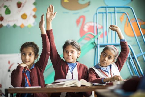 Three children in class holding up their hands