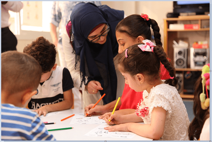 Teacher in Lebanon with primary children at a table with work sheets and coloured pencils