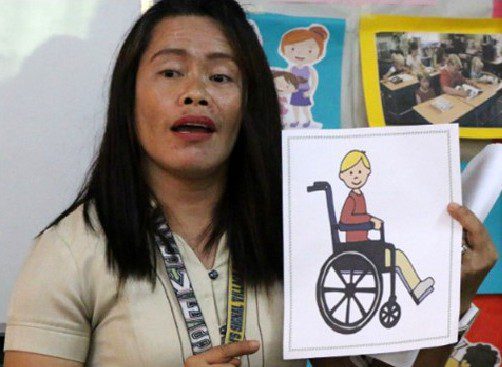 teacher holding up a picture of a child in a wheelchair