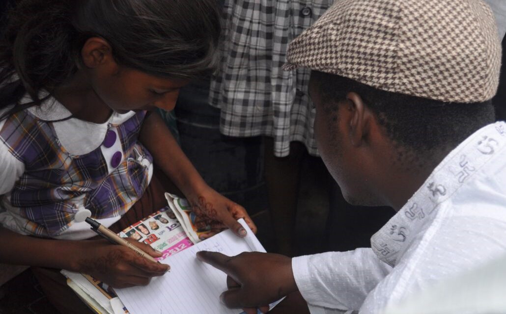 man wearing a flat hat, explaining to a child who is writing