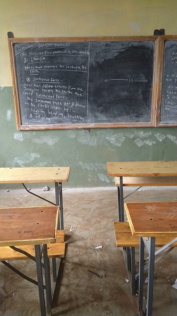 Blackboard at the front of empty desks and chairs in a class