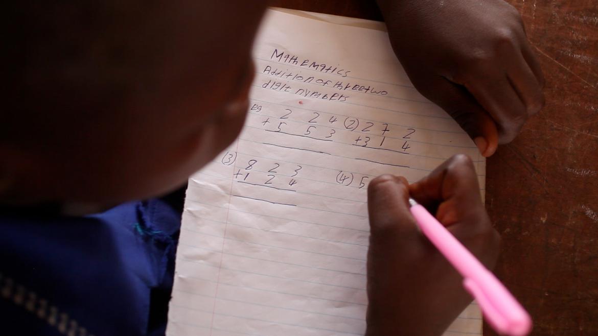 student working on addition of three and two digit numbers holding a pink pen