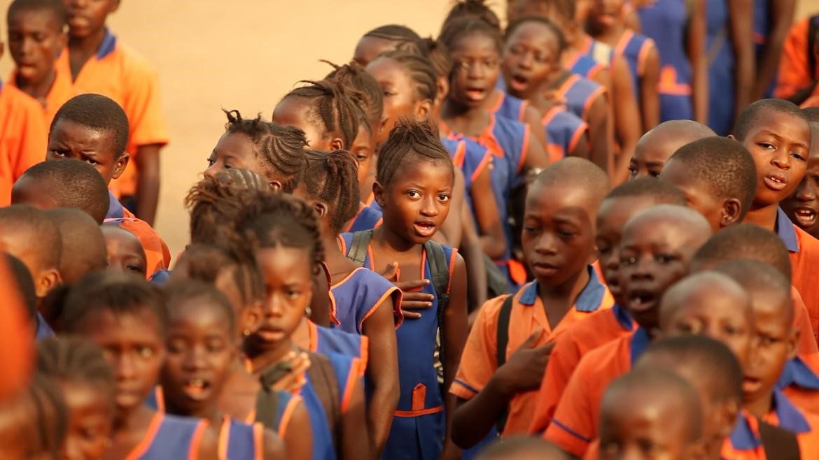 Children waiting in line in a school in Sierra Leone.  Orange and blue uniforms