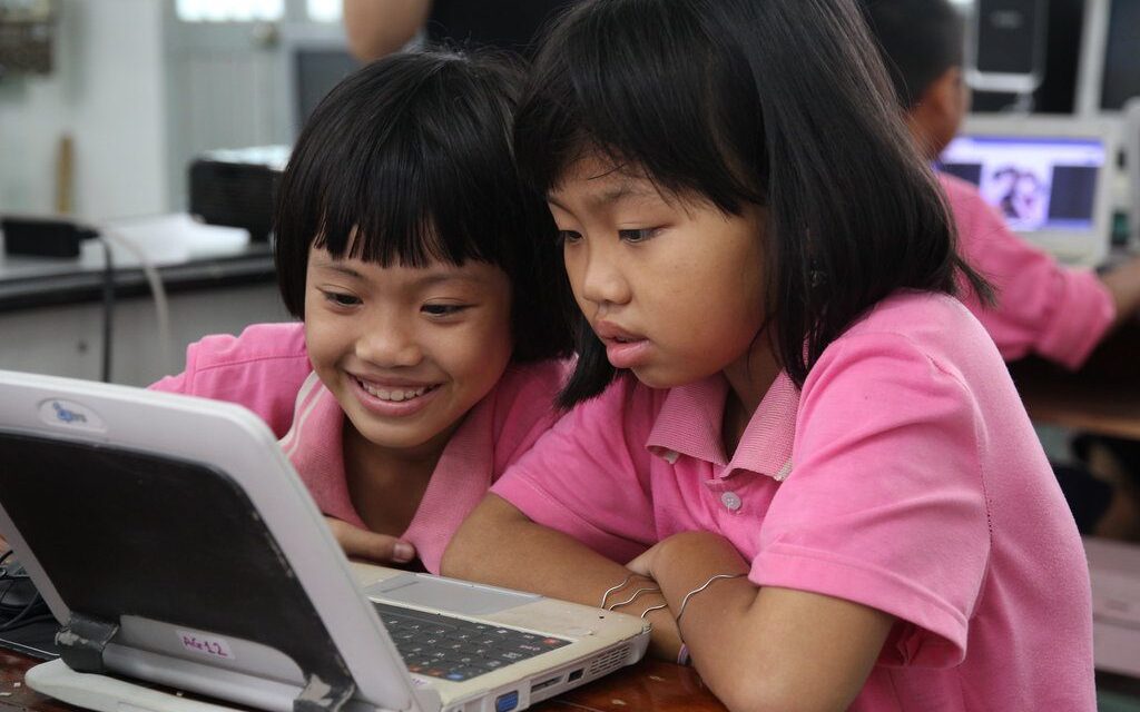 Two asian primary school age girls in pink t shirts looking at a laptop