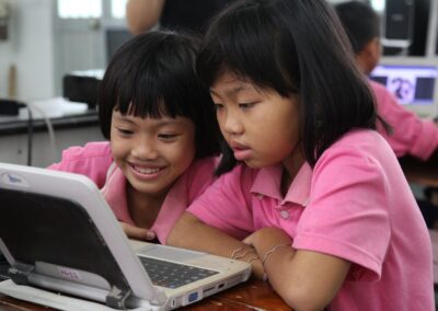 Two asian primary school age girls in pink t shirts looking at a laptop