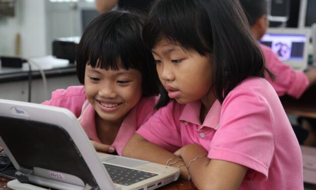 Two asian primary school age girls in pink t shirts looking at a laptop