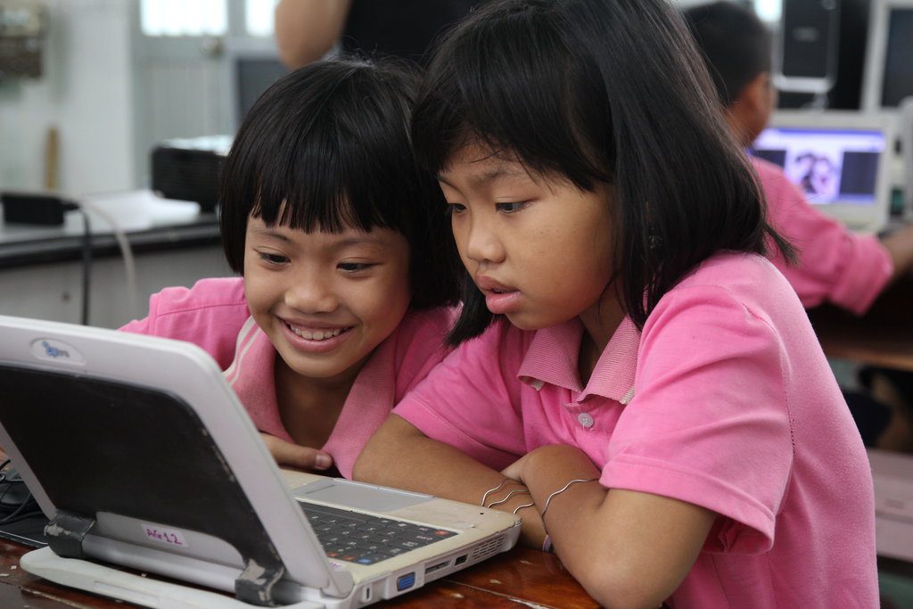 Two asian primary school age girls in pink t shirts looking at a laptop
