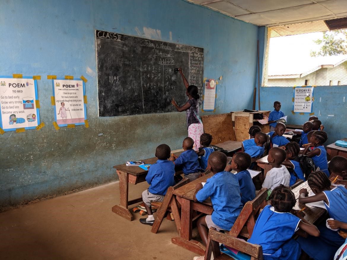 African teacher at blackboard in class of primary school children in blue uniforms