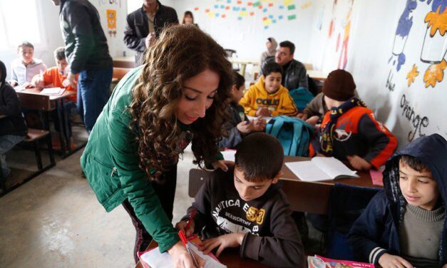 teacher marking work at desk with children in class