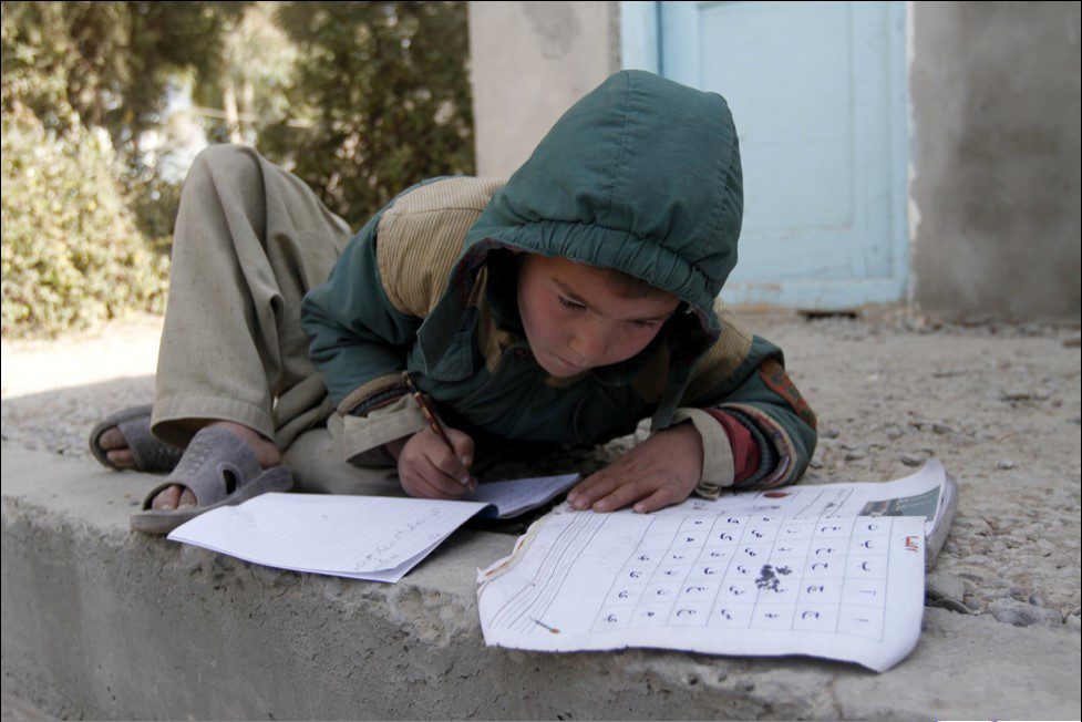 Boy in a coat with hood up working outside on school work