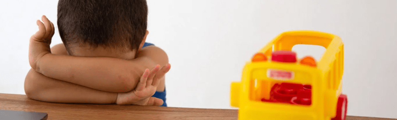 Pre primary child with head in his arms alongside a yellow plastic school bus