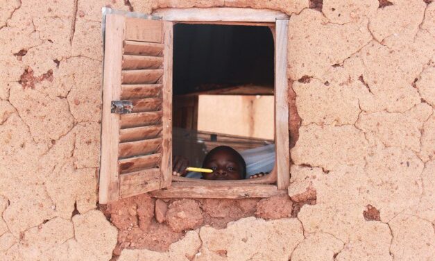 A Ghanaian boy peeks out of the window with his new mosquito net in the background