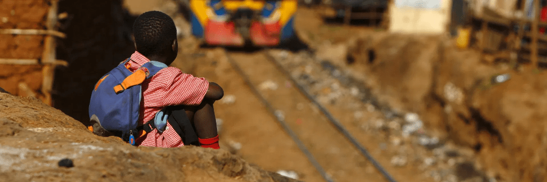 primary age child sitting by the side of a railway track with train approaching