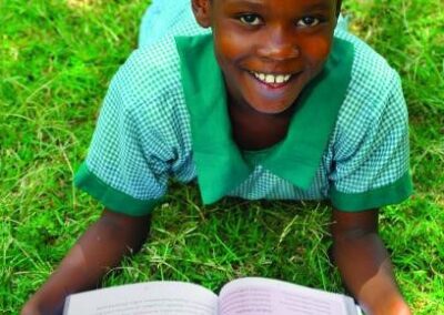 School girl in green uniform lying on her front on grass reading a book