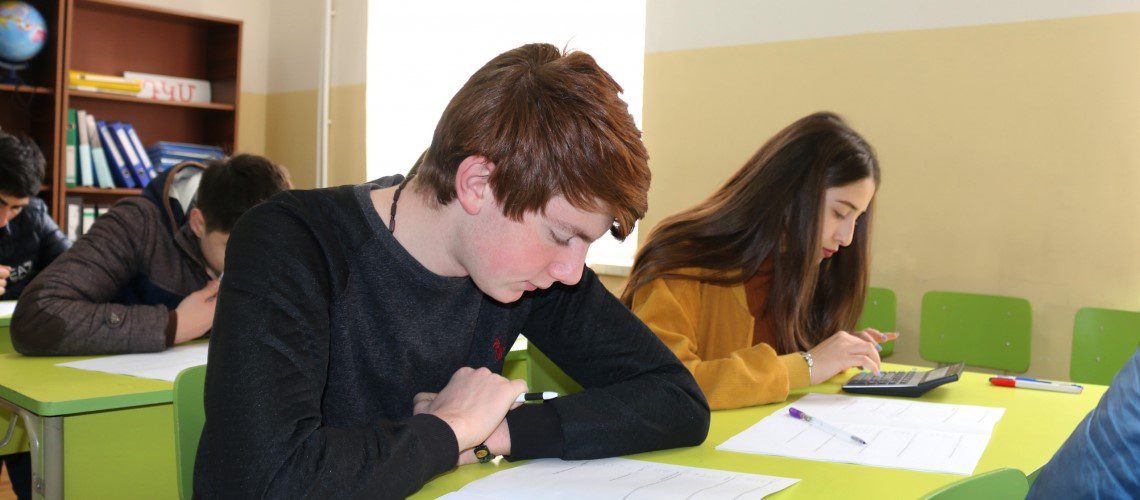 Students in class with green desks and chairs