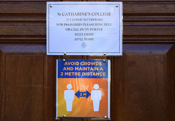 Notice on a panelled wooden door "St Catherine's College is closed to visitors for deliveries please ring the bell or call duty porter 0223 338300 07711 783000 below that is an orange and blue sign Avoid crowds and maintain a 2 metre distance illustrated by two people shapes with an arrow between them and 2M