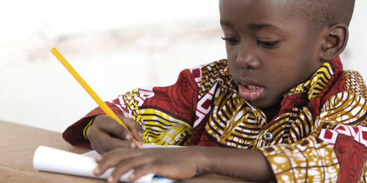 Primary age african boy writing with a yellow pencil