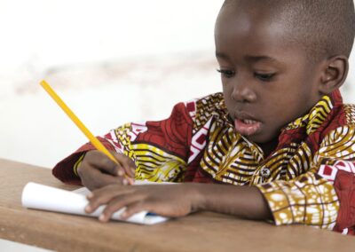 Primary age african boy writing with a yellow pencil