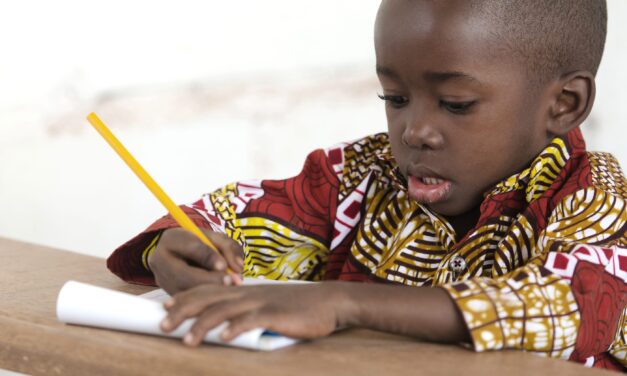 Primary age african boy writing with a yellow pencil