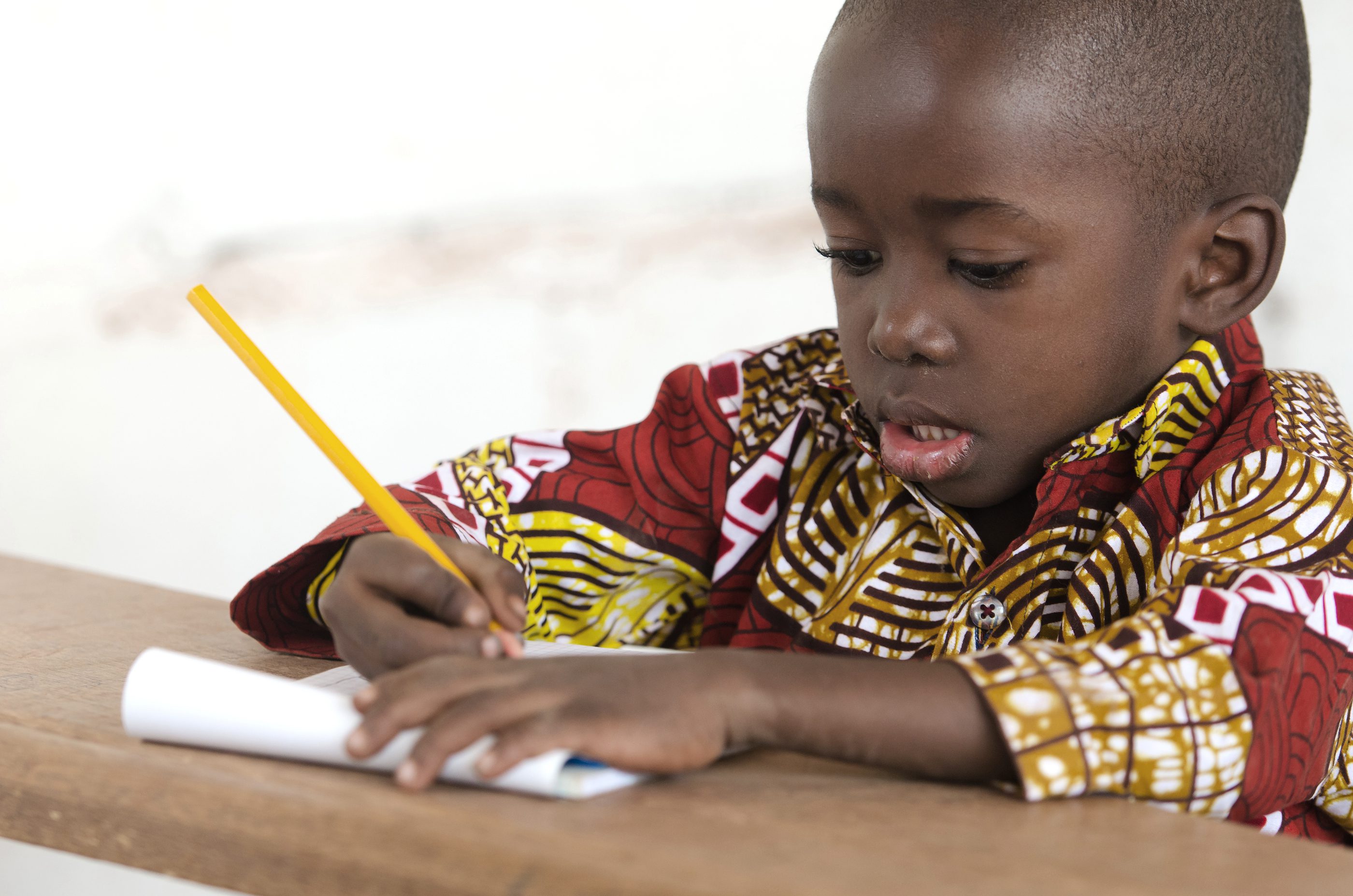 Primary age african boy writing with a yellow pencil
