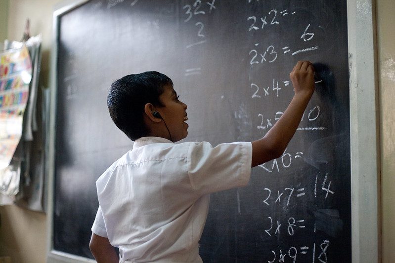 Sri Lankan boy with hearing aids working on maths problem at a classroom blackboard