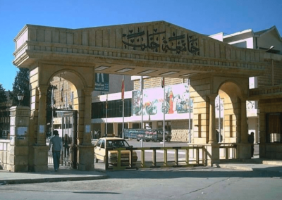 University of Aleppo - Archway with barriers and car and flagpoles beyond