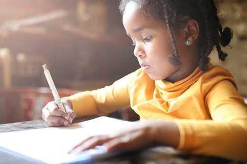 Primary age African girl in yellow jumper writing 