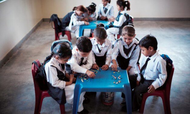 primary age children sitting around two tables making patterns with crayons