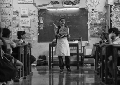Black and white photo of teacher at front of classroom with an atlas