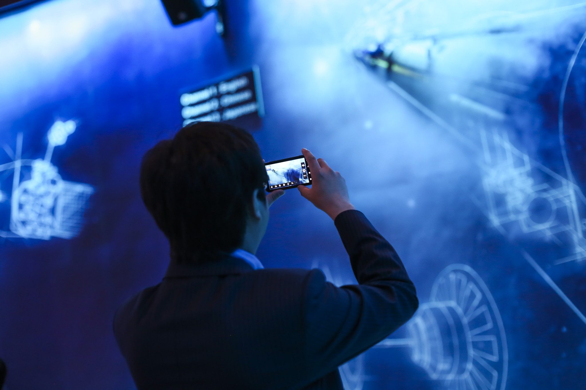 Man taking a photo with a mobile phone of a blue coloured digital wall